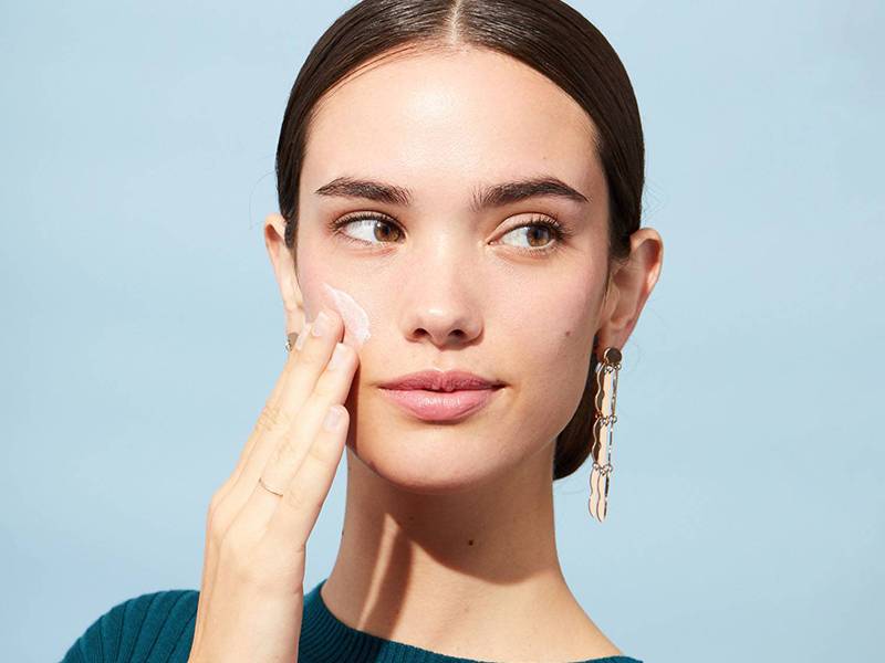 Person putting cream on face on blue background